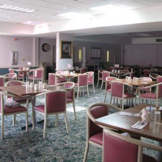 An empty dining hall with arranged tables and chairs, bathed in natural light.
