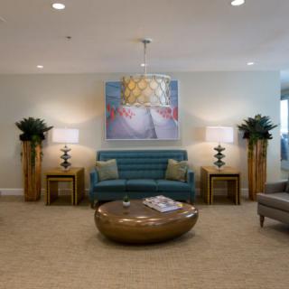 A well-furnished lobby with a sofa, round table, artwork, and decorative lamps.