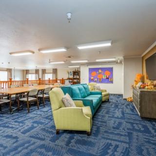 A spacious living room with colorful sofas, a long dining table, and vibrant artwork on the wall.