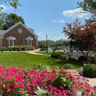 A serene outdoor scene featuring vibrant flowers, a charming building, and a tranquil lake under a clear blue sky.