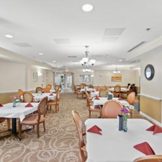 A well-lit dining room with elegantly set tables, featuring red napkins and comfortable chairs.