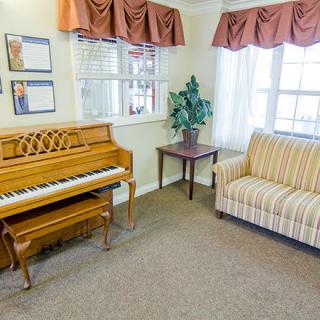 A cozy living room featuring a piano and sofa next to windows with curtains.