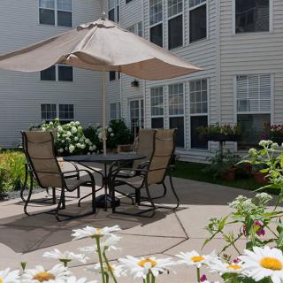 A cozy patio setup with chairs and an umbrella surrounded by blooming flowers beside a building.