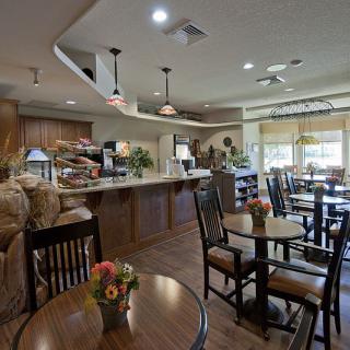 A cozy cafe interior with neatly arranged tables and chairs, a service counter, warm lighting, and decorative elements.