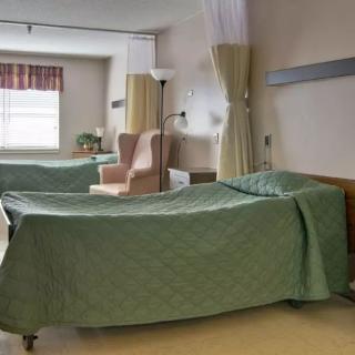 A hospital room with two neatly made beds, separated by privacy curtains.