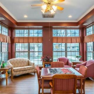 A cozy living room with abundant natural light, featuring a mix of comfortable seating and a table set, highlighted by large windows and warm wooden flooring.