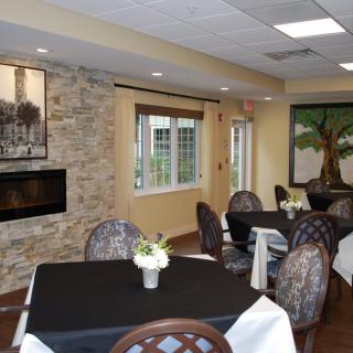 A cozy dining room with neatly arranged tables and chairs, featuring a fireplace and decorative artwork on the walls.