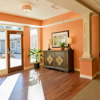 A warmly lit lobby entrance with wooden flooring, a decorative cabinet, and indoor plants.