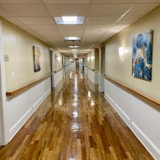 A long, well-lit hallway featuring polished wooden floors and framed artwork along the walls.