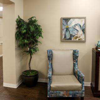 A cozy corner featuring a patterned chair, a decorative plant, and artwork on the wall.