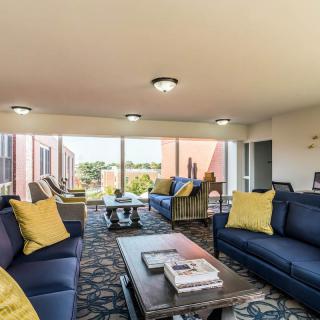 A modern living room with blue sofas, yellow pillows, large windows, and a coffee table.