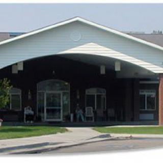 The image shows the entrance of a building with a prominent gable roof and large windows.