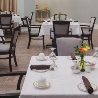 A neatly arranged dining area with tables set for guests, featuring floral centerpieces.