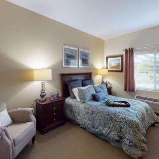A cozy bedroom with a bed, two lamps, and a comfortable chair by the window.