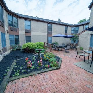 A serene courtyard featuring a brick pathway, garden beds, and outdoor seating with umbrellas.