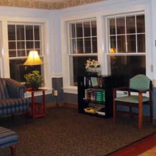 A cozy living room with comfortable chairs, a lamp, and large windows.