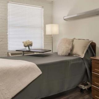 A cozy bedroom with a neatly made bed, lamp, and a side table.