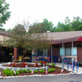 The entrance of a school building with landscaped greenery and a tree in the foreground.