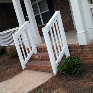 A small porch entrance with white railings and brick stairs.
