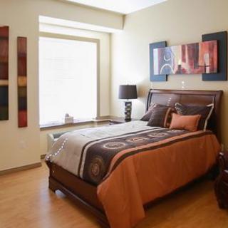 A cozy bedroom featuring a wooden bed with brown and orange bedding, complemented by wall art and a bedside lamp.