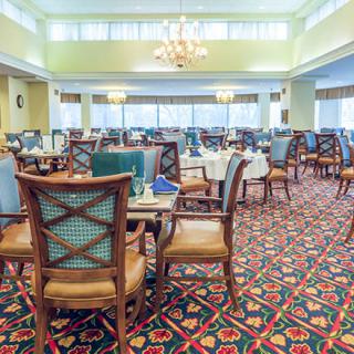 An elegant dining area with wooden chairs, round tables, and a patterned carpet under bright lighting.