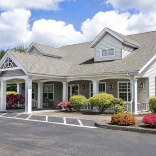 A charming white building with a landscaped garden and colorful flowers under a bright blue sky with clouds.