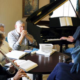 A group of musicians gathered around a piano, collaborating and rehearsing together.