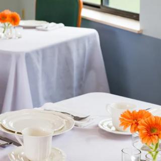 A neatly set dining table with white tablecloths and orange flowers as decoration.