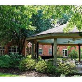 A peaceful garden setting with a gazebo and a brick building in the background.
