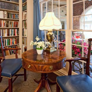 A cozy reading nook with a wooden table, chairs, and a well-stocked bookshelf.