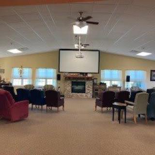 A spacious living area with a projector screen, fireplace, and rows of chairs.