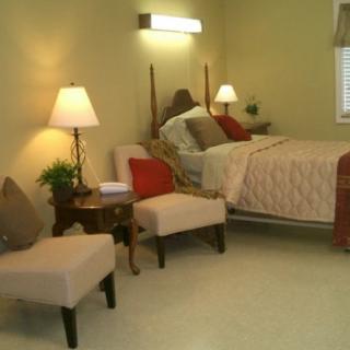 A cozy bedroom with a neatly made bed, two chairs, and ambient lighting from lamps.