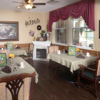 A cozy dining room with neatly set tables and a fireplace, featuring elegant decor and large windows.