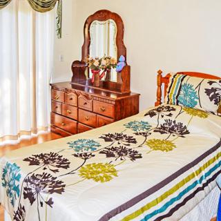 A cozy bedroom with a single bed featuring floral bedding, alongside a wooden dresser and mirror.