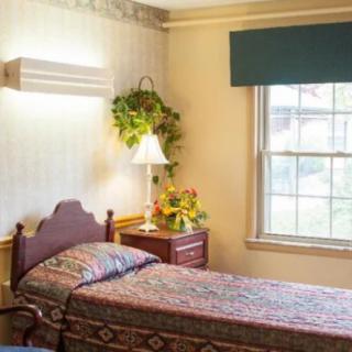 A cozy bedroom with a single bed, nightstand, and floral decorations by the window.