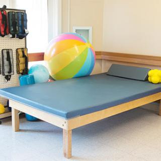 A therapy room equipped with a therapeutic mat and playful items, including a colorful beach ball.