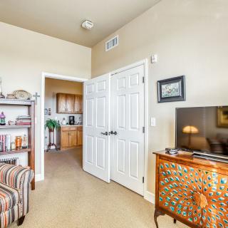 A cozy living room with a television, bookshelf, and striped armchair near an open doorway leading to the kitchen.