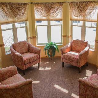 A cozy sitting area with four armchairs arranged around a central plant, bathed in sunlight from large windows.