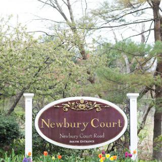 Welcome sign for Newbury Court, surrounded by blooming nature.