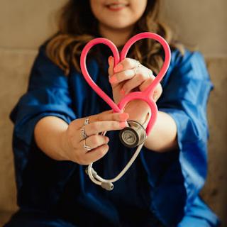 A healthcare professional creatively forms a heart shape with a pink stethoscope, symbolizing care and compassion.