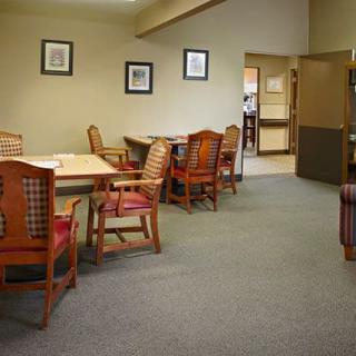 An empty dining room with wooden chairs and tables, adorned with framed paintings on the walls.