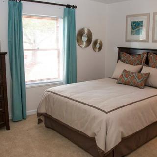 A neatly arranged bedroom with a bed, bedside tables, and teal curtains framing a window.