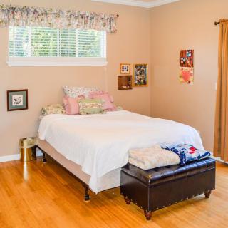 A cozy bedroom with a neatly made bed and decorative pillows, featuring warm colors and hardwood flooring.