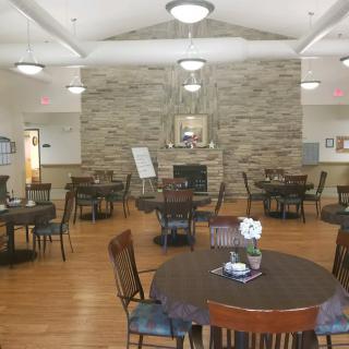 A cozy dining area with round tables, chairs, and a stone fireplace.
