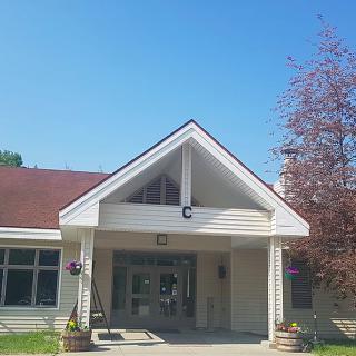 A quaint building with a peaked roof and entrance, surrounded by greenery under a clear blue sky.