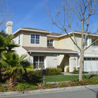A two-story suburban house with a well-maintained lawn and surrounding trees.