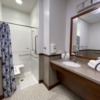 A well-lit and spacious bathroom featuring a shower area, vanity with sink, and neatly arranged towels.
