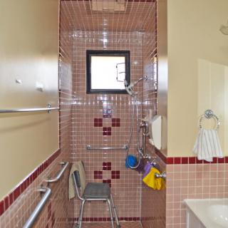 A bathroom with red tiled shower area equipped with a shower chair and grab bars.