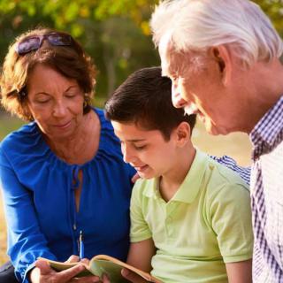 A child reading a book with their grandparents in a park.
