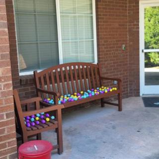 A wooden bench covered with colorful toy eggs on a patio.